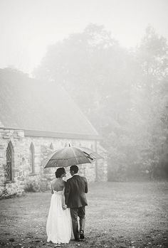 a man and woman standing under an umbrella in front of a stone church on a foggy day