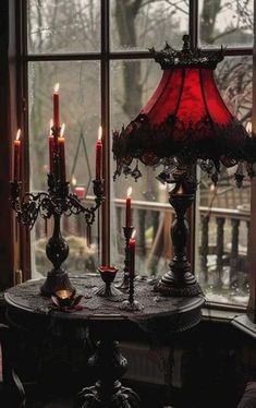 a table with candles and a red lamp on it in front of a large window