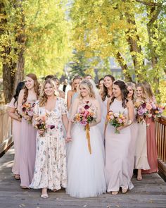 a group of women standing next to each other on a wooden bridge holding bouquets