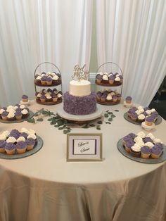 a table topped with lots of cupcakes covered in purple and white frosting