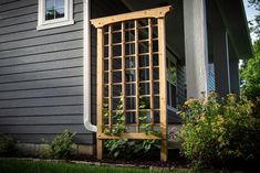 a wooden trellis sitting on the side of a house next to a green bush