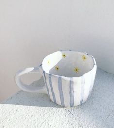 a white and blue striped coffee cup sitting on top of a cement slab next to a wall