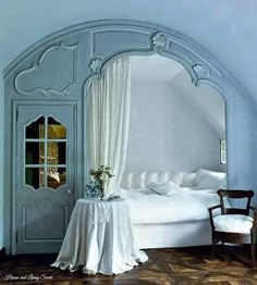 a white bed sitting in a bedroom next to a window with curtains on top of it