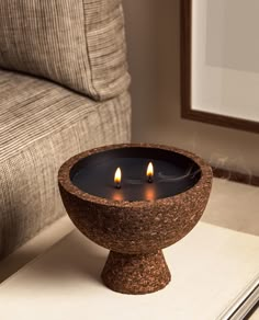 two lit candles sit in a stone bowl on a table next to a couch and chair