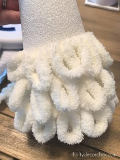 a close up of a toilet paper holder on a wooden table with a hand holding it