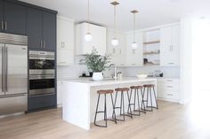 a kitchen with white cabinets and wooden flooring has three stools in front of the island