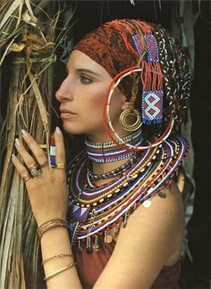 a woman with many bracelets and rings on her head, leaning against a tree