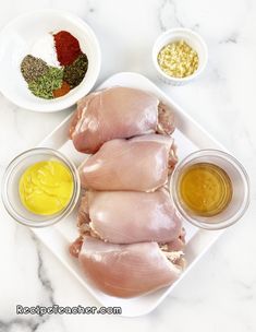 raw chicken on a plate with seasonings, spices and salt in small white bowls