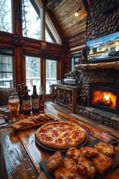 a table with pizza and beer on it in front of a fire place that is built into the wall