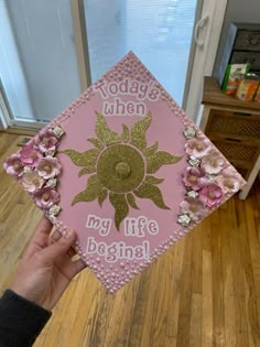 someone is holding up a pink graduation cap with flowers on it that says today is when my life begins