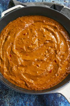 a pan filled with sauce sitting on top of a blue tablecloth next to a knife and fork