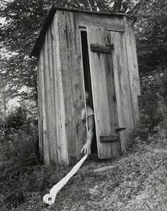 an outhouse in the woods with a hose coming out of it's door