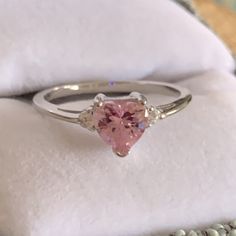 a pink heart shaped diamond ring sitting on top of a white cloth next to some beads