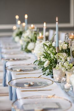 a long table is set with white flowers and silverware, candles and plates on it