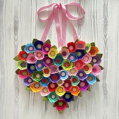 a heart shaped origami decoration hanging on a white wooden wall with pink ribbon