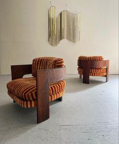 an orange and white striped chair sitting in front of a wall with two wooden chairs next to it