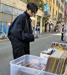 a man standing next to a bin full of records on the side of a road