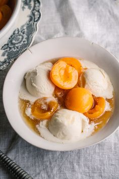 a white bowl filled with ice cream and oranges next to a cup of tea