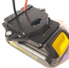 a black and yellow device on a white surface with some wires attached to the back