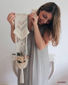 a woman holding up a macrame hanging from a chair with flowers on it