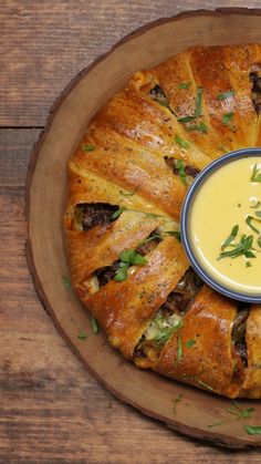 a wooden plate topped with a pastry covered in cheese and garnished with herbs