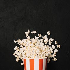 an orange and white striped bucket full of popcorn on a black background with copy space