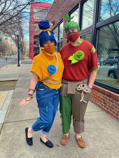 two people in costume standing next to each other on the sidewalk near a store front