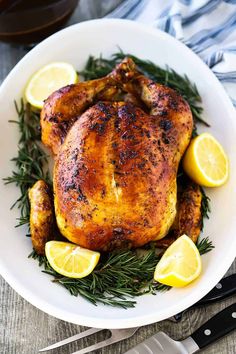 a roasted chicken with lemons and rosemary on a white plate next to a knife and fork