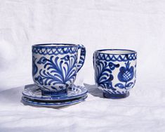 two blue and white cups sitting next to each other on top of a tablecloth