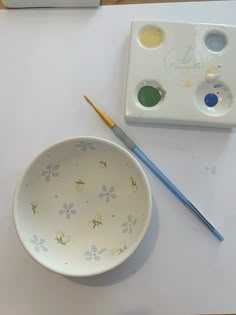 a bowl and paintbrush sitting on a table next to a white box with flowers painted on it