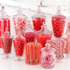 many different types of candies in glass vases on a white counter top with candy canes and lollipops