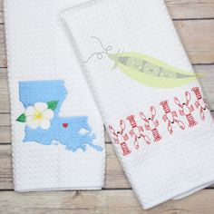 two white towels with designs on them sitting next to each other in front of a wooden table