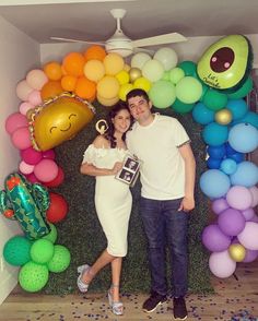 a man and woman standing in front of a balloon arch with balloons on the wall