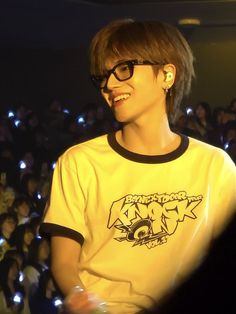 a young man with glasses standing in front of an audience at a music concert, smiling