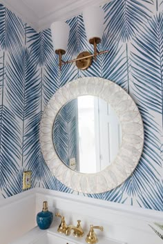 a bathroom with blue and white wallpaper, gold faucets and a round mirror