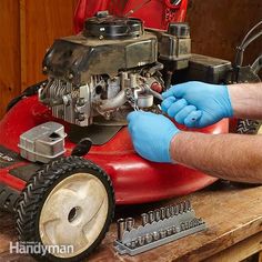 a man in blue gloves working on a red lawn mower