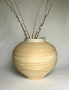 a white vase with some branches in it on a tableclothed surface, ready to be used as a centerpiece