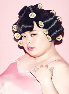 a woman with curlers in her hair posing for a photo against a pink background