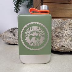 a flask shaped like a canister with an orange clip on the top and a tree in the background