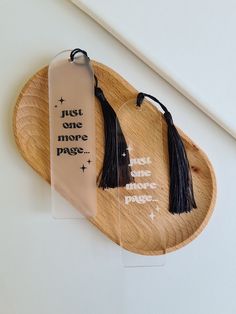 two bookmarks with tassels on them sitting on a wooden platter that says just one more page