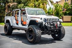 a white jeep with orange accents is parked in a parking lot next to some trees