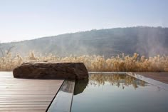 a large rock sitting on top of a wooden deck next to a pool in front of a mountain