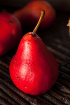 two red pears sitting next to each other on a wooden table with brown stems