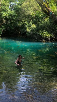 a woman wading through a river surrounded by green trees and blue - colored water