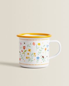 a yellow rimmed mug with flowers painted on the outside and inside, sitting on a white surface