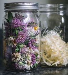 two jars filled with flowers sitting on top of a counter next to another jar full of dried flowers