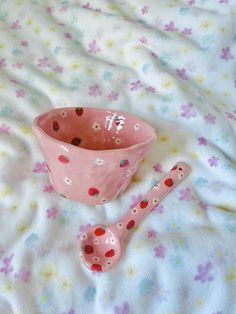 a pink bowl and spoon sitting on top of a white bed covered in stars print sheets