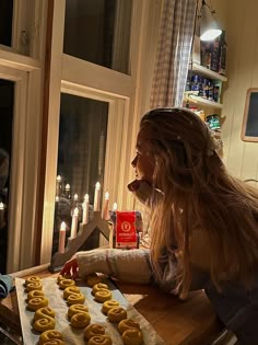 a woman sitting at a table in front of a tray of doughnuts with candles behind her