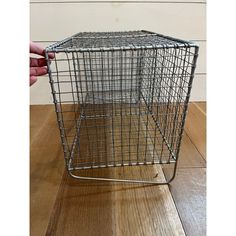 a hand holding a metal cage on top of a wooden floor