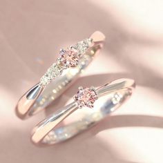 two wedding rings with diamonds on them sitting next to each other in front of a pink background